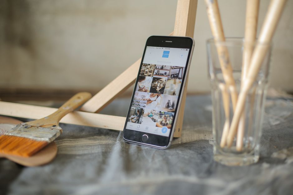 Modern smartphone displaying images amidst artist brushes and easel.