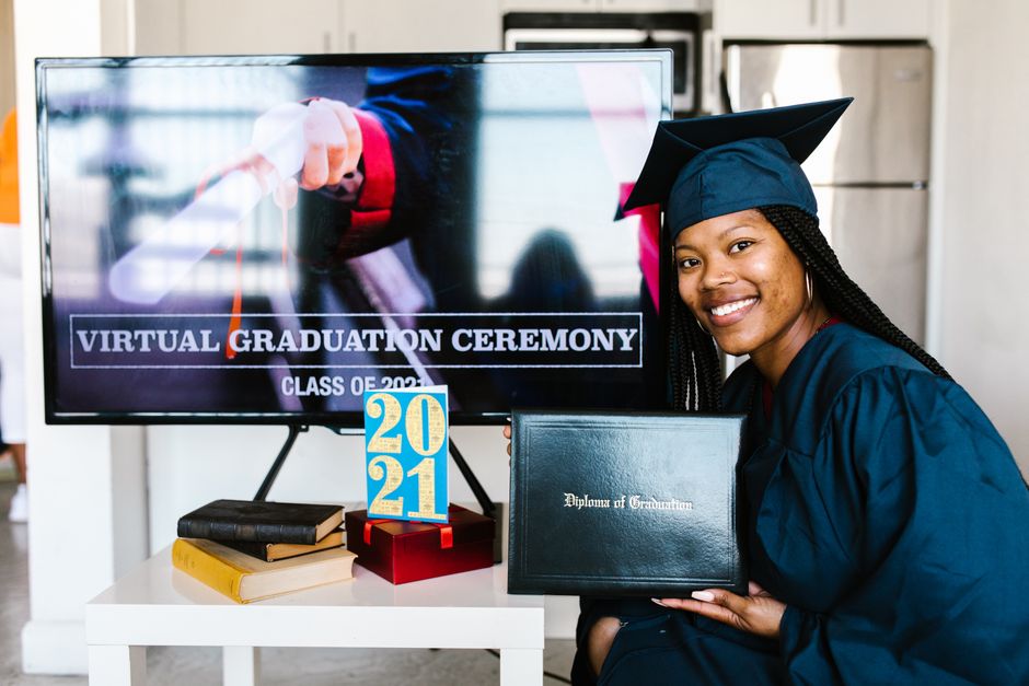 A joyful virtual graduation ceremony with a smiling graduate holding a diploma in front of a TV.